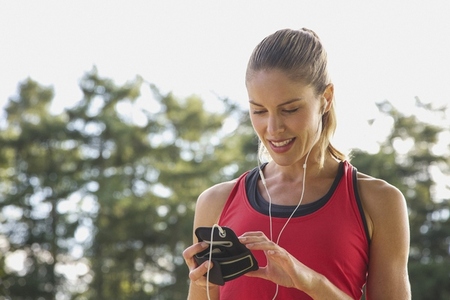 Blond female runner with headphones looking down at smart phone