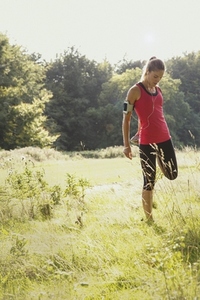 Female runner with headphones stretching leg in sunny