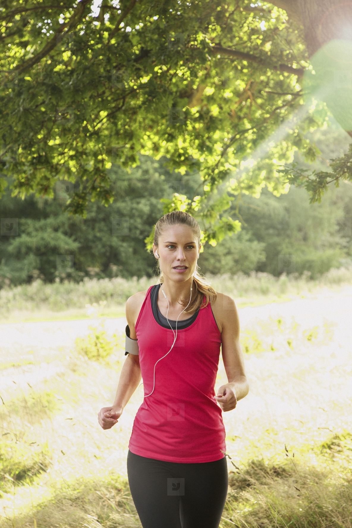Beautiful blond woman with headphones and arm band running in sunny grassy park