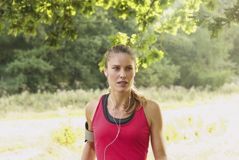 Beautiful blond woman with headphones and arm band running in sunny grassy park