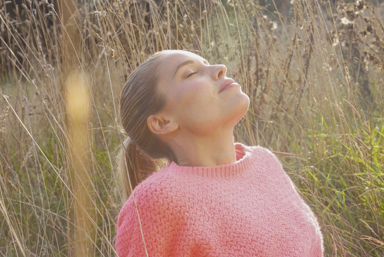 Beautiful serene woman in pink sweater sitting in tall grassy meadow