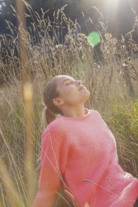 Beautiful serene woman in pink sweater sitting in tall grassy meadow