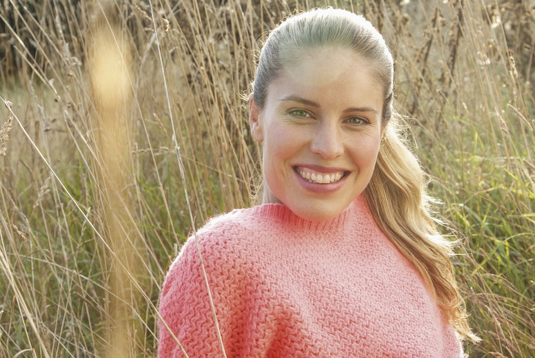 Portrait of beautiful blond woman in pink sweater sitting in sunny tall grass