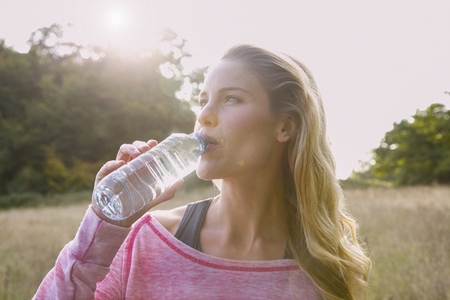 Beautiful thoughtful blond woman drinking from water bottle in sunny rural field
