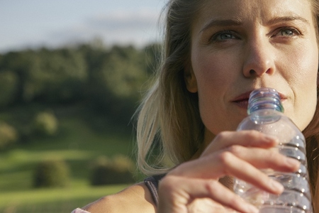 Close up portrait of beautiful thoughtful woman drinking from plastic water bottle in sunlight Close up portrait of beautiful thoughtful woman drinking from plastic water bottle in sunlight
