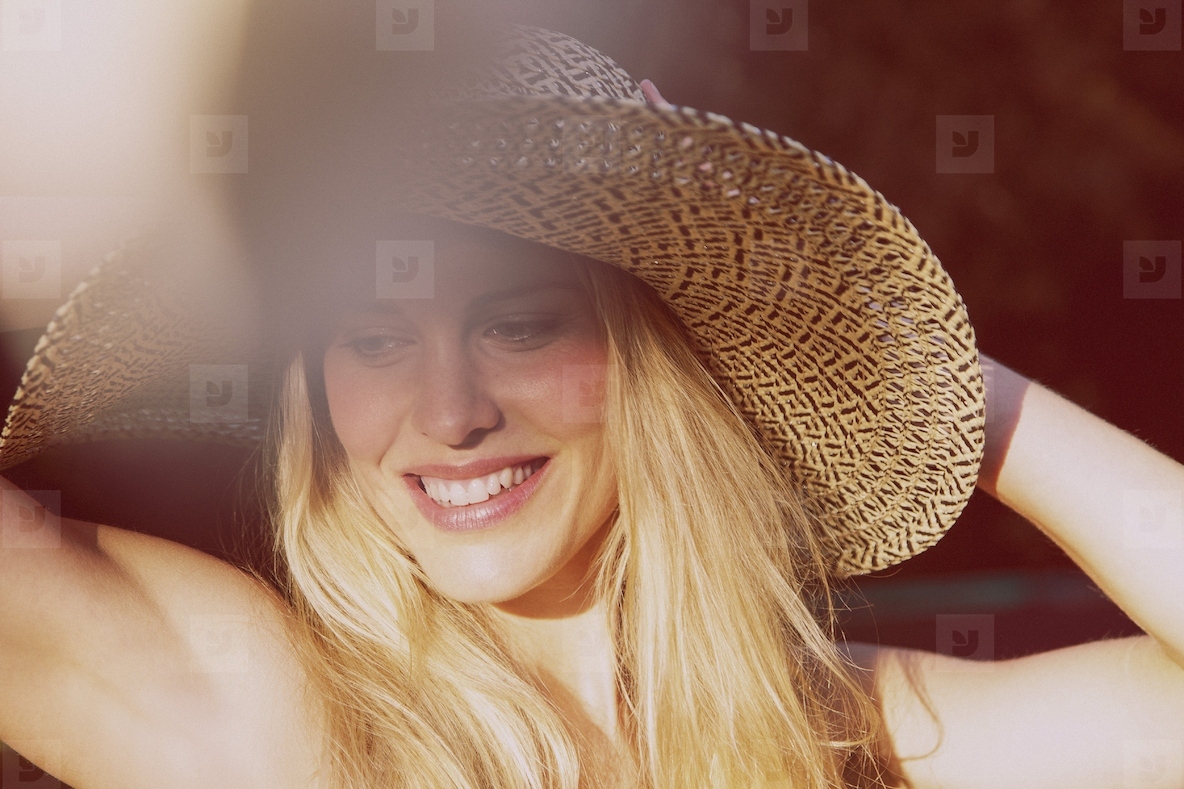 Beautiful blond woman in sun hat smiling and looking down in sunlight