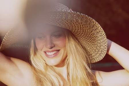 Beautiful blond woman in sun hat smiling and looking down in sunlight