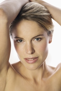 Close up studio portrait of beautiful blond woman with bare shoulders and arms raised