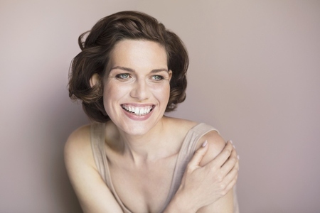 Portrait of happy beautiful young brunette woman smiling and looking away against pink background