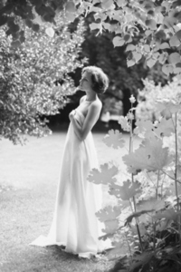 Beautiful tall serene woman wrapped in white sheet standing in summer garden and looking away