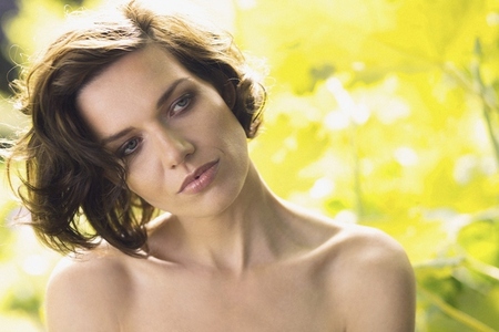 Portrait of serene woman with short brown hair and bare shoulders looking away in sunny garden