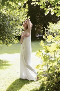 Portrait of beautiful woman wrapped in gauzy fabric standing in sunlight in summer garden