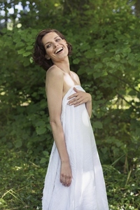 Portrait of happy carefree young woman in strapless white dress laughing in summer woods