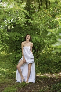 Portrait of tall carefree beautiful woman in strapless dress standing among green leaves in woods