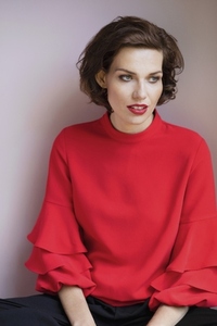 Studio portrait of beautiful young brunette woman in red blouse with ruffled sleeves looking away