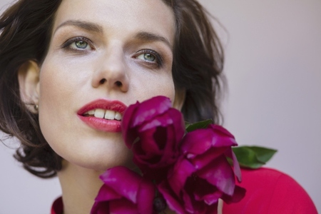 Close up portrait of beautiful brunette woman with blue eyes holding dark pink flowers Close up portrait of beautiful brunette woman with blue eyes holding dark pink flowers