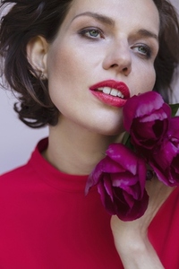 Close up portrait of beautiful brunette woman holding dark pink flowers and looking away