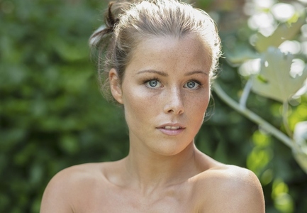 Portrait of beautiful wide eyed young woman with bare shoulders and freckles in summer garden