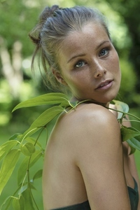 Portrait of beautiful young woman with green leaves draped over bare shoulder in summer garden