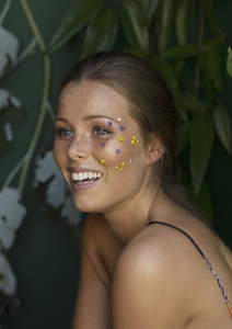 Portrait of happy young woman with purple and yellow flower petals on face smiling and looking away