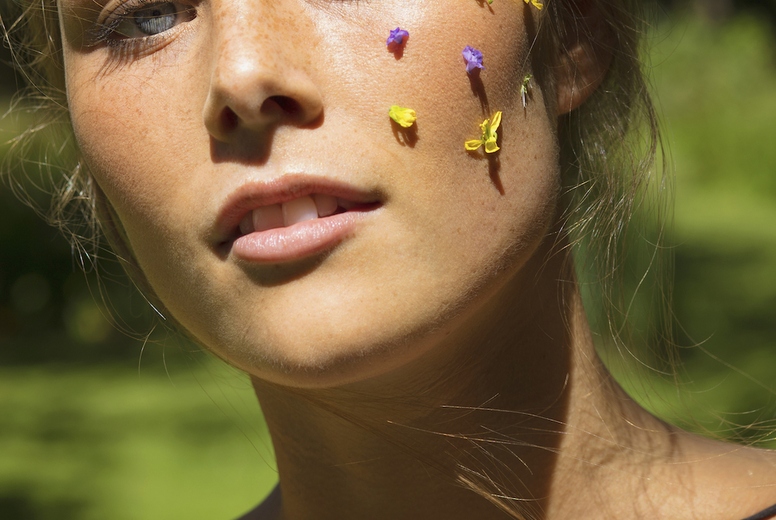 Close up portrait of beautiful young woman with purple and yellow flower petals on face
