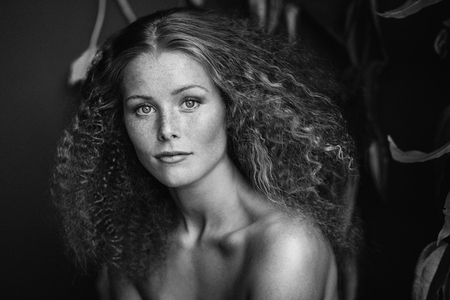 Black and white portrait of confident beautiful young woman with curly hair and bare shoulders