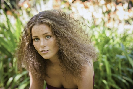 Portrait of beautiful young woman with curly brown hair and blue eyes in summer garden Portrait of beautiful young woman with curly brown hair and blue eyes in summer garden