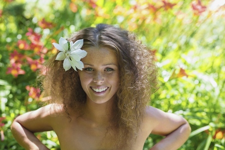 Portrait of beautiful young woman with bare shoulders in tropical garden with flower in curly hair Portrait of beautiful young woman with bare shoulders in tropical garden with flower in curly hair