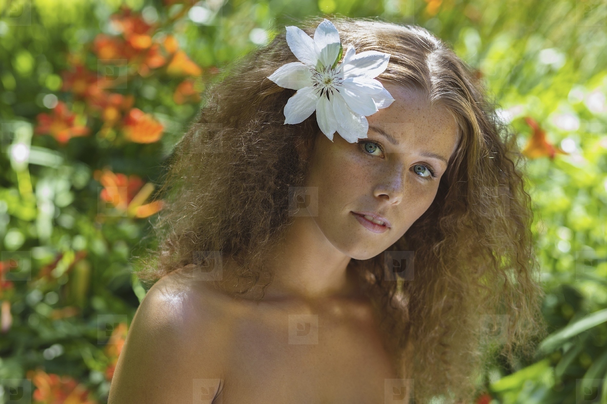 Portrait of beautiful young woman with bare shoulders and tropical white flower in curly brown hair