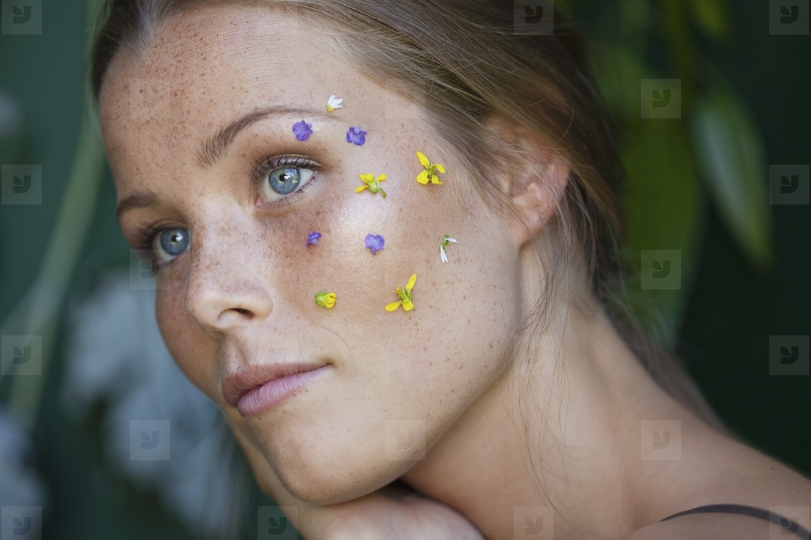 Close up portrait of thoughtful young woman with blue eyes and flower petals on face looking away