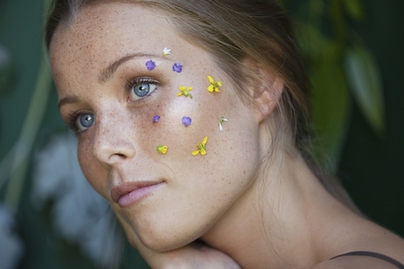 Close up portrait of thoughtful young woman with blue eyes and flower petals on face looking away
