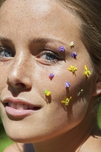 Close up portrait of smiling young woman with purple and yellow flower petals on face in sunlight Close up portrait of smiling young woman with purple and yellow flower petals on face in sunlight