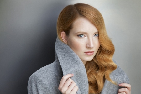Formal portrait of beautiful stylish young redhead woman holding collar against gray background