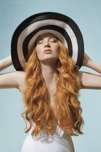 Studio portrait of young woman with long curly red hair with striped sun hat and eyes closed