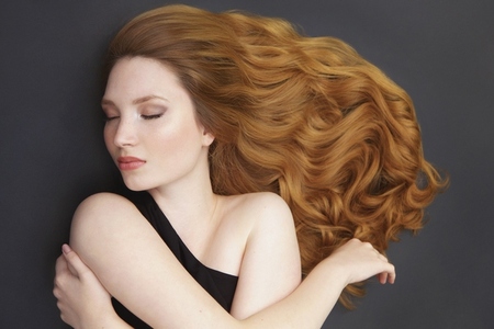 Portrait of beautiful serene young woman with long curly hair spread over gray background