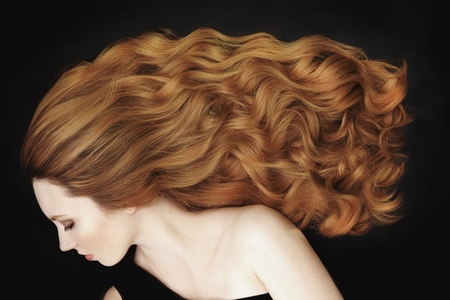 Studio portrait of beautiful young woman with long curly red hair against black background