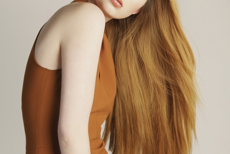 Formal portrait of beautiful stylish young woman with long red hair in orange dress