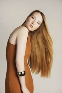 Formal portrait of beautiful stylish young woman with long red hair in orange dress