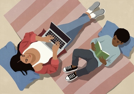 View from above of mother working at laptop next to son reading book on living room floor