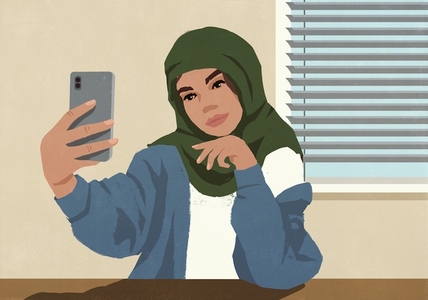 Young Muslim woman in hijab taking selfie with smart phone