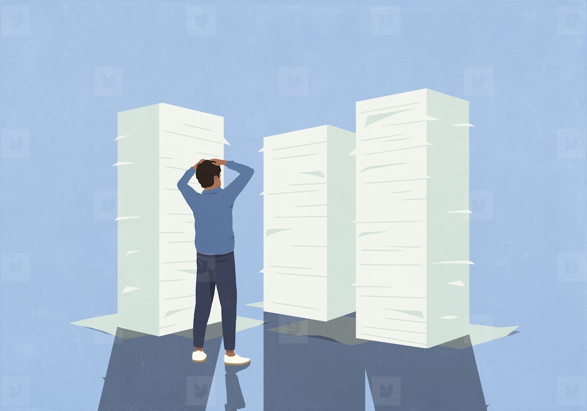 Overwhelmed man with hands on head looking at large stacks of paperwork