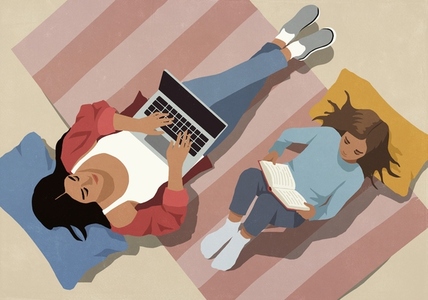 View from above of mother working at laptop next to daughter reading book on floor at home