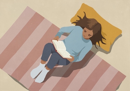 View from above of girl relaxing laying on rug and pillow reading book