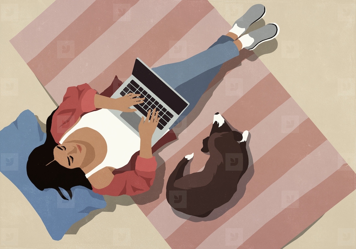 View from above of dog laying on rug next to woman using laptop at home