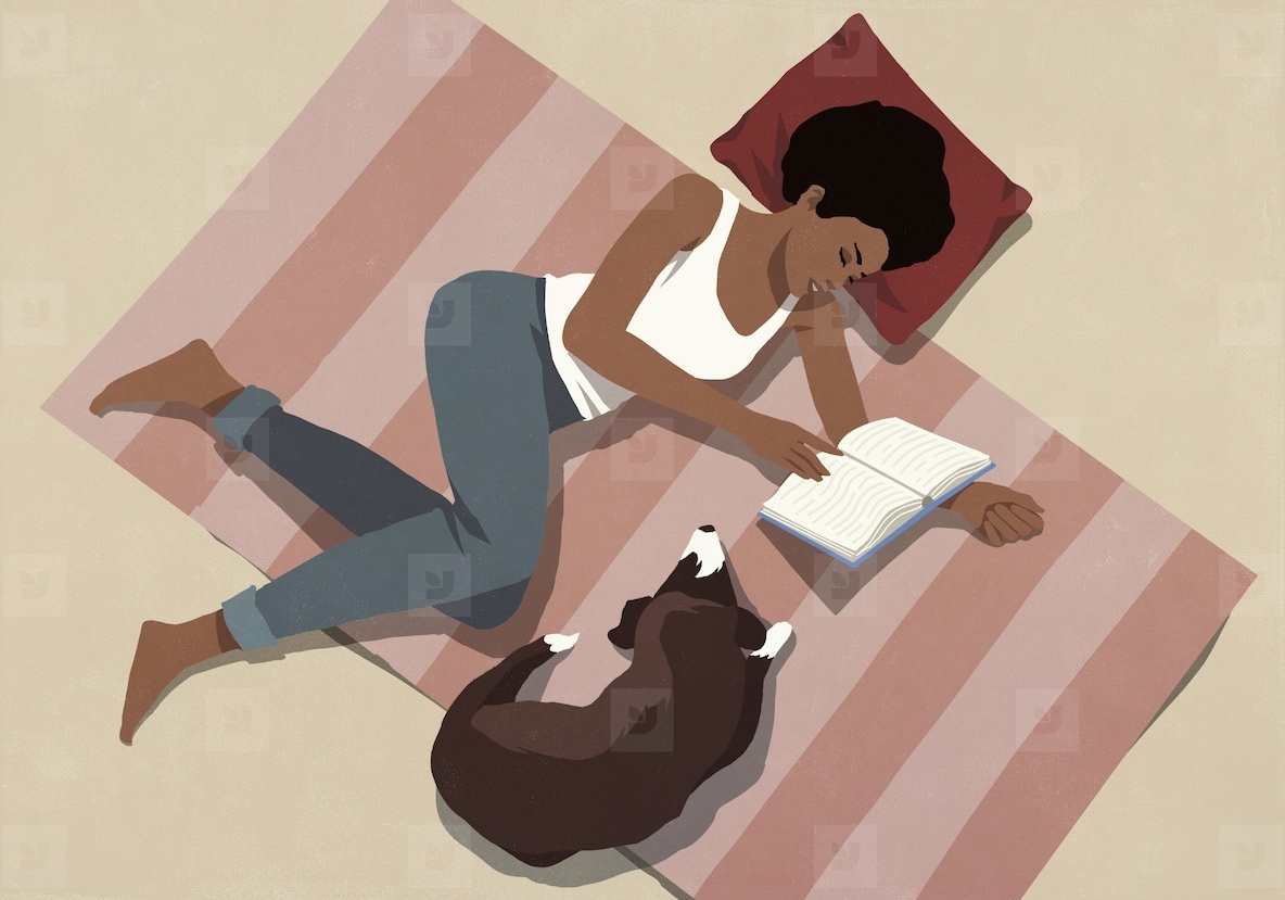 View from above of woman relaxing at home reading book on floor next to dog