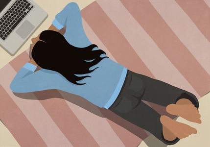 View from above of barefoot woman relaxing laying on rug using laptop at home