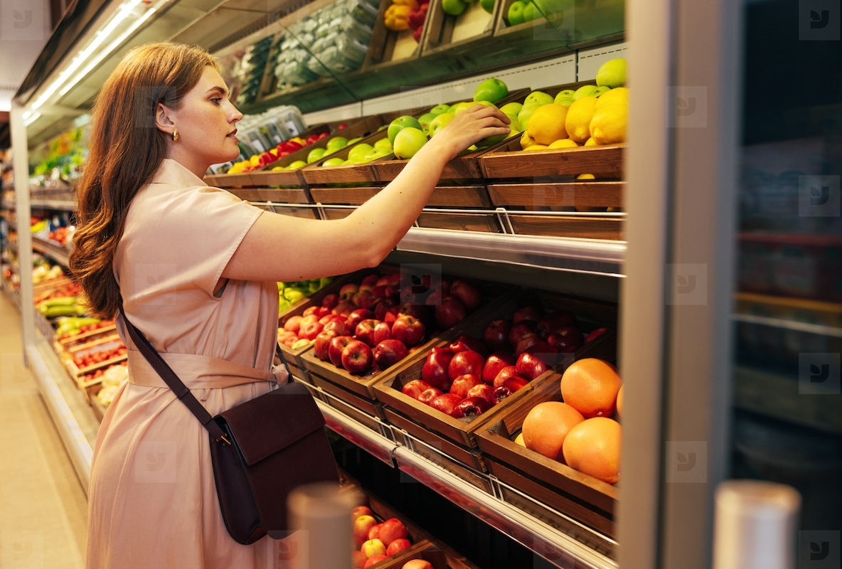 Young woman customer takes out a green apple from the shelf in the grocery store