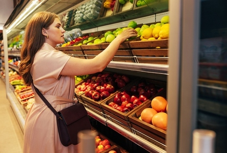 Young woman customer takes out a green apple from the shelf in the grocery store Young woman customer takes out a green apple from the shelf in the grocery store