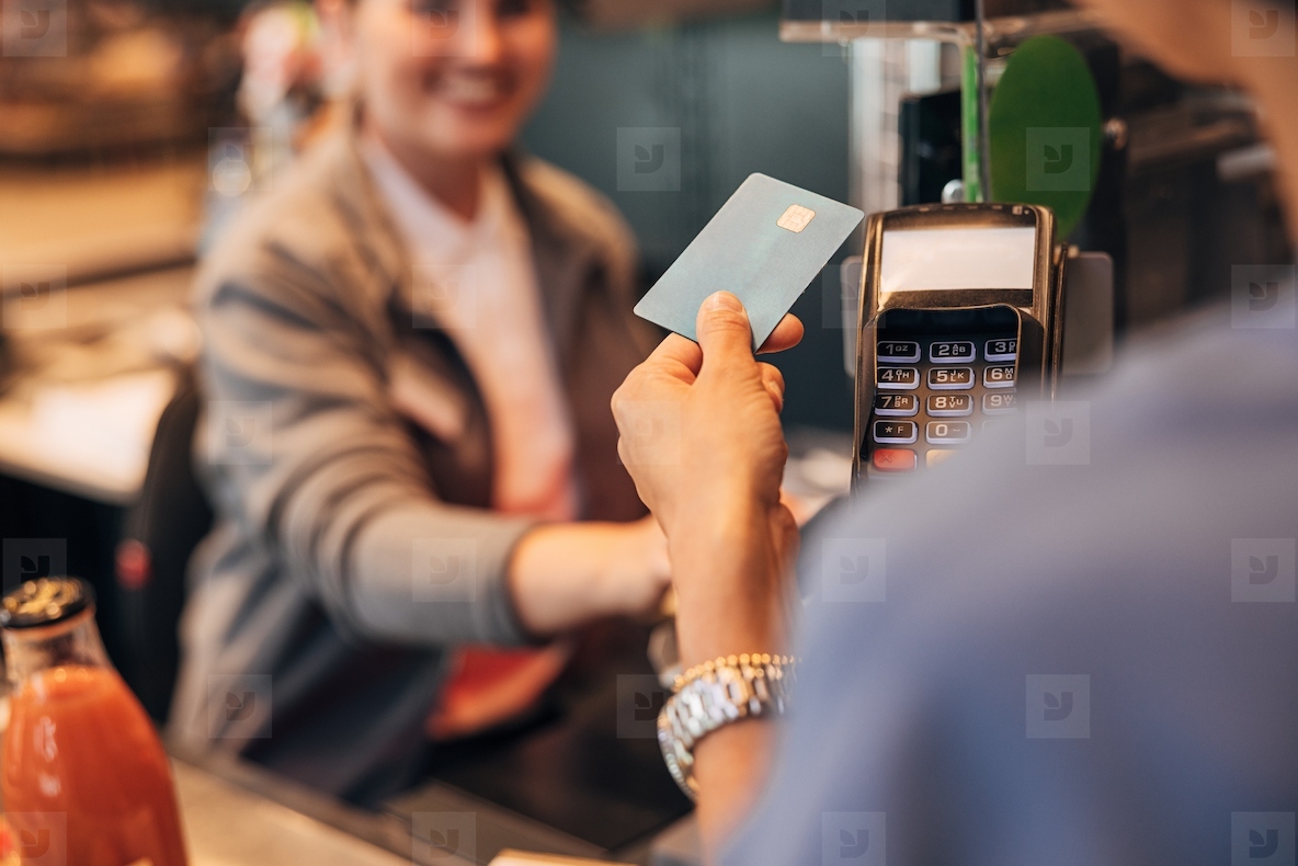 View from the shoulder of the customer paying by card at pos terminal in a grocery store