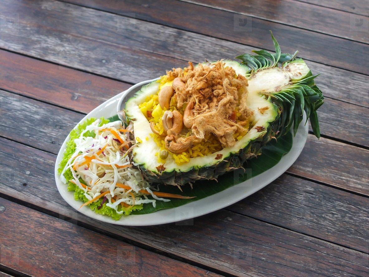 Thai style pineapple fried rice served in a pineapple on a woode
